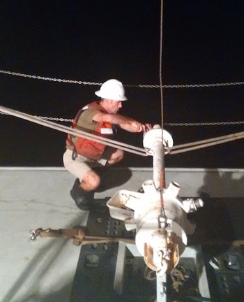 The wax-tipped corer is used to collect volcanic glass samples from the bottom of the ocean. It is an example of how safety and scientific goals go hand in hand. The corer weighs about 200 kilograms and requires working close to the stern of the ship, so a helmet, steel-toed boots, and a life vest must be worn. The picture shows Ronald Spelz securing the wax cups to the end of the sampler.