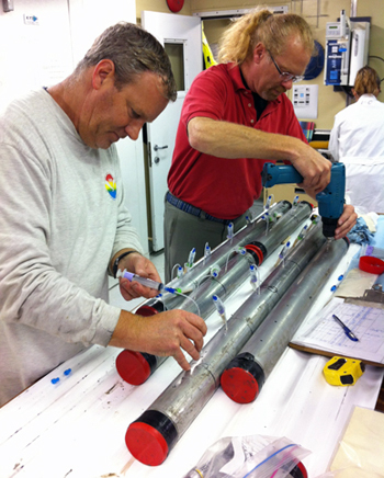 Pete Dartnell (left) inserts tubing attached to a syringe to extract pore water from a vibracore while Tom Lorenson (right) drills a hole in the core so the pore water can be extracted from that core.
