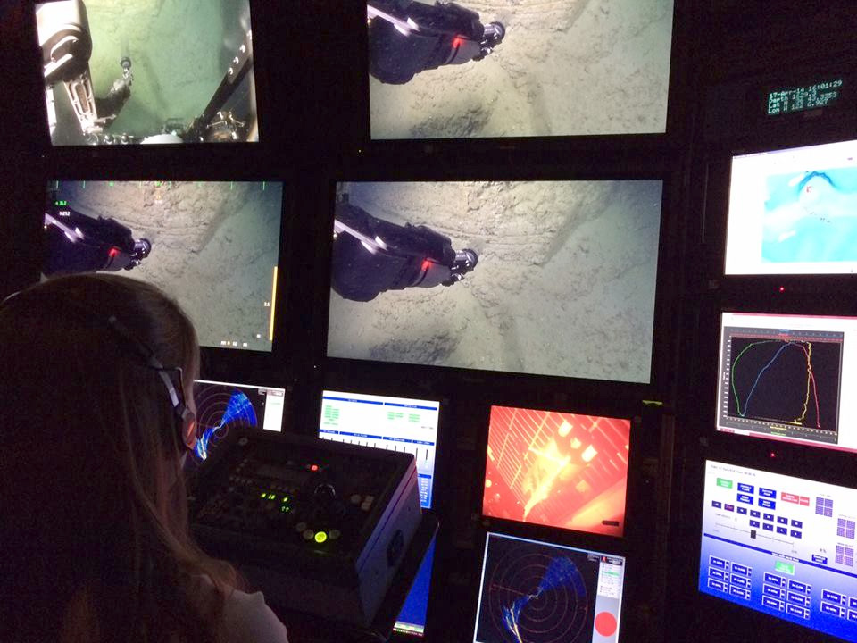 Katie Coble from the US Geological Survey controls the science camera on ROV Doc Ricketts from the Western Flyer control room. The video screens show the ROV manipulator collecting a
