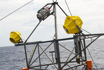 The time-lapse camera contained within a titanium cylinder is mounted at the top of the tripod frame and pointed down toward the seafloor. The system is programmed take a picture every hour. The strobe lights on either side flash simultaneously to illuminate the pitch-black seafloor.