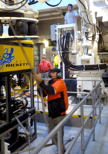 ROV Pilot Ben Erwin pulls the recovery line off the crane as Chief Mate Erik Larson operates the crane.