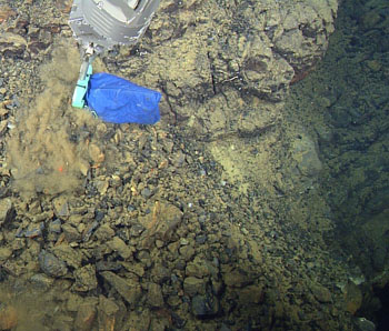 A sample of gravel-sized talus from a fault scarp on the rhyolite dome is collected with a scoop-bag.