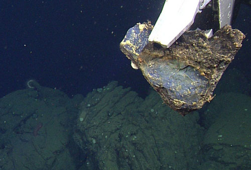 The manipulator arm holds a sample from “bread crust”-like pillows, with iron-oxidation on the outside and a noticeable blue cast on freshly broken surfaces. These characteristics lead us to suspect that this is a high-silica lava.