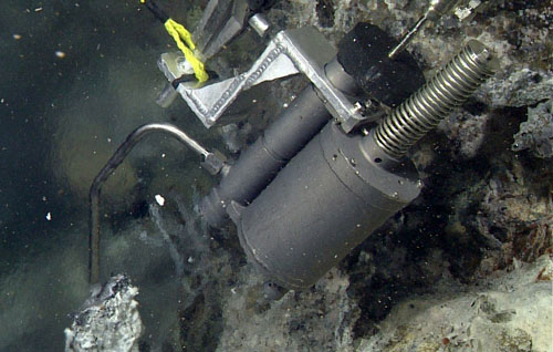 Collecting water from a chimney venting clear shimmering hydrothermal fluids. The nozzle has to be positioned fully into the orifice, but visibility is often poor. The pilots operate the ROV’s robotic arm nearly 3,700 meters below us while looking at monitors displaying views from several camera angles to accomplish this difficult three-dimensional task.