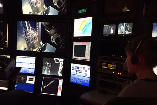 Lauren Shumaker watches as the ROV pilot uses the manipulator arm to open the drawer on the ROV sled. The vibracorer is mounted on the front of the vehicle, which you can see on the main monitor.