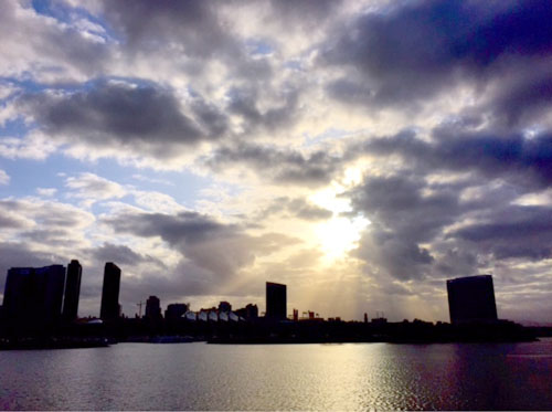 The sun peeks through clouds over downtown San Diego as the Western Flyer leaves San Diego Bay.