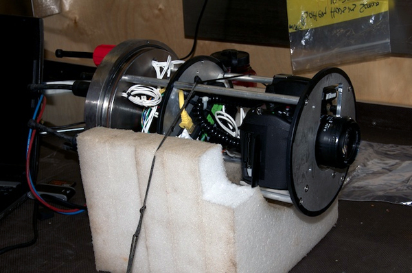 The insides of the time-lapse camera system. The canister houses a digital SLR camera and circuitry to allow pictures to be downloaded without removing the camera or memory card. Cables exit the back of the housing through special water-tight connectors. All of this is enclosed in a cylindrical titanium housing that was pressure-tested to 6,000 meters or about 9,000 pounds per square inch of pressure. When mounted on the camera frame, the cables run down from the camera to another pressure-rated housing that contains a bank of lithium batteries and a specialized microcontroller board that operates the camera and two separate strobe lights.