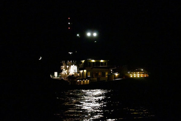A waxing crescent moon shines on Lone Ranger as seen from the small tender boat at night.