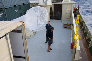 Don Montague and Joe Brock move the kytoon into the tan science van for protection from gusting winds. They have kept the kytoon inflated in anticipation of using it again and to maximize a limited supply of helium needed to replenish it. Photo: Debbie Nail Meyer