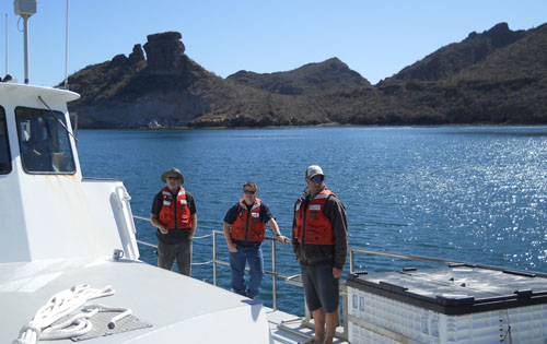 Perry Shoemake, Jim Boedecker, and Paul Ban stand on deck as the Zephyr nears port in San Carlos on the mainland of Mexico near Guaymas.
