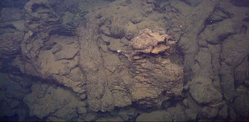 Contact between several different units. The elongate pillow lavas flowed around the collapsed sheet flow (which had left the horizontal shelves as it drained and its flow surface dropped). This shows that the pillow lava flow occurred after the sheet flow formation and collapse.