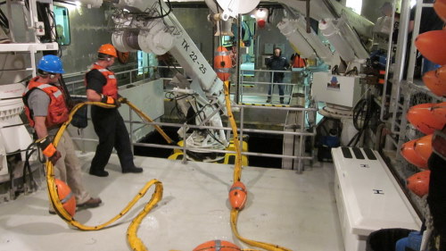 Crew members Cole Davis and Jason Jordan hoist up the tether during an ROV recovery as the pilots watch the vehicle come up through the moon pool.
