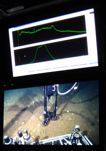 The two key monitors to watch in the control room while running the laser Raman spectrometer. The lower monitor shows the probe on the seafloor in its stabilizing tripod. The upper monitor shows the spectra returned from the laser system; each peak indicates a different chemical signal.