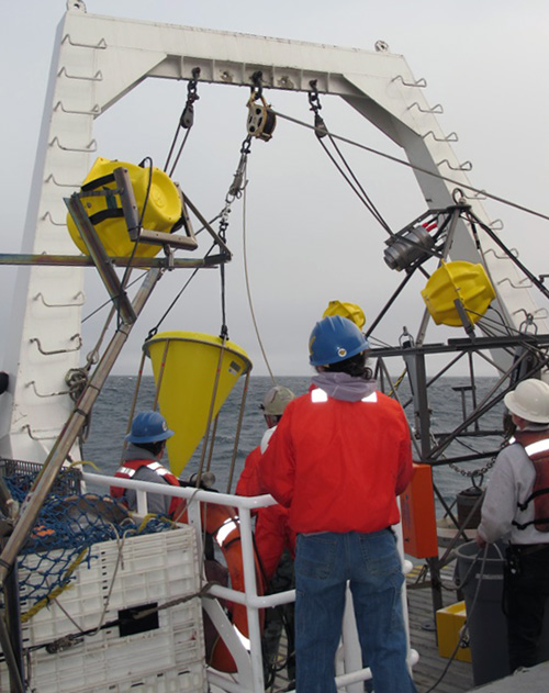 The first sediment trap is redeployed. The entire mooring—floats, lines, and all—is about 800 meters (half a mile) long and takes about two hours to place carefully into the water. Each instrument needs to be staged on deck and deployed in a specific order. The last item to go in the water is the camera tripod (on the right).