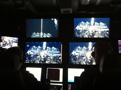 This image from the ROV control room shows ROV pilot Randy Prickett (left) hooking the Midwater Respirometry System (MRS) onto an attachment point on the ROV. He then slid the MRS off the hanger and backed away from the mooring.