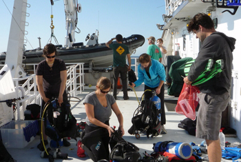 The blue-water divers assemble their gear on the back deck. The ship's crew prepares the small boat for launch.