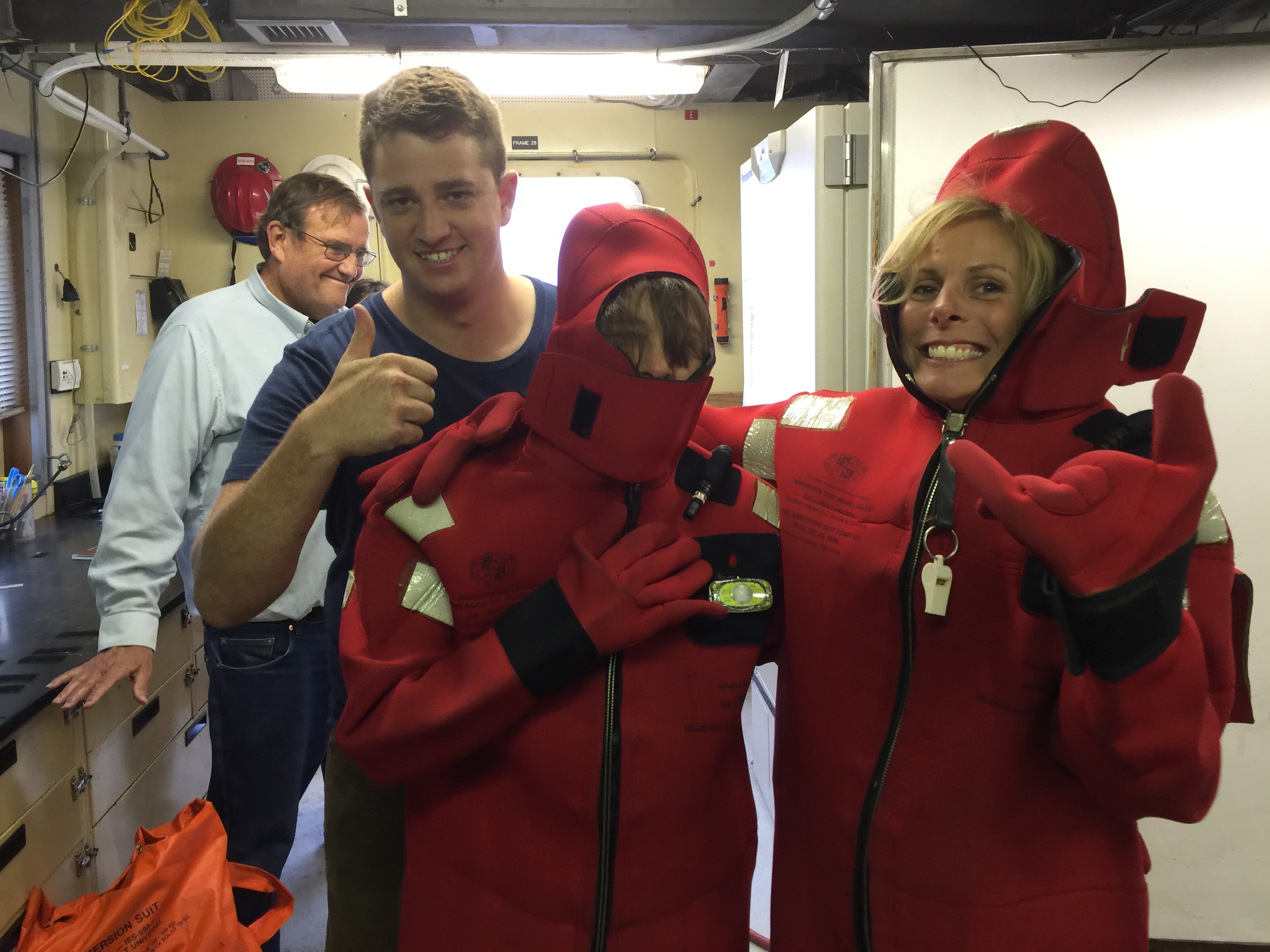 Second Mate Trevor giving Kris Walz and Shannon Johnson tips on how to get their immersion suits fully zipped up during our safety briefing. Jim McClain is photobombing behind them.