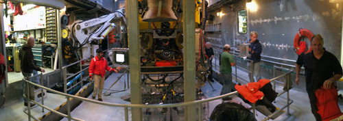 Panorama of the moonpool after the ROV recovery. Crew, pilots, and scientists are all busy when the ROV comes on deck. Pilots secure the ROV and then, with the help of crew, prepare the tether for the next deployment while the science team unloads samples.