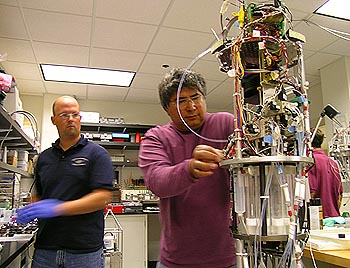 The Environmental Sample Processor (ESP) is a unique instrument that can detect specific types of microscopic plants and animals in seawater by analyzing their DNA. In this photograph, MBARI researchers Joe Jones (left) and Roman Marin III (right) prepare the ESP for deployment in Monterey Bay. Photo: Kim Fulton-Bennett (c) 2004 MBARI