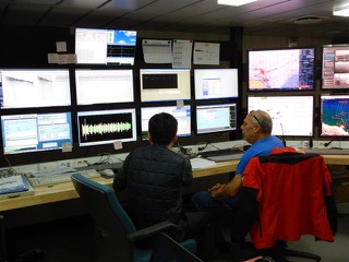 Scientists watching an array of computer monitors.