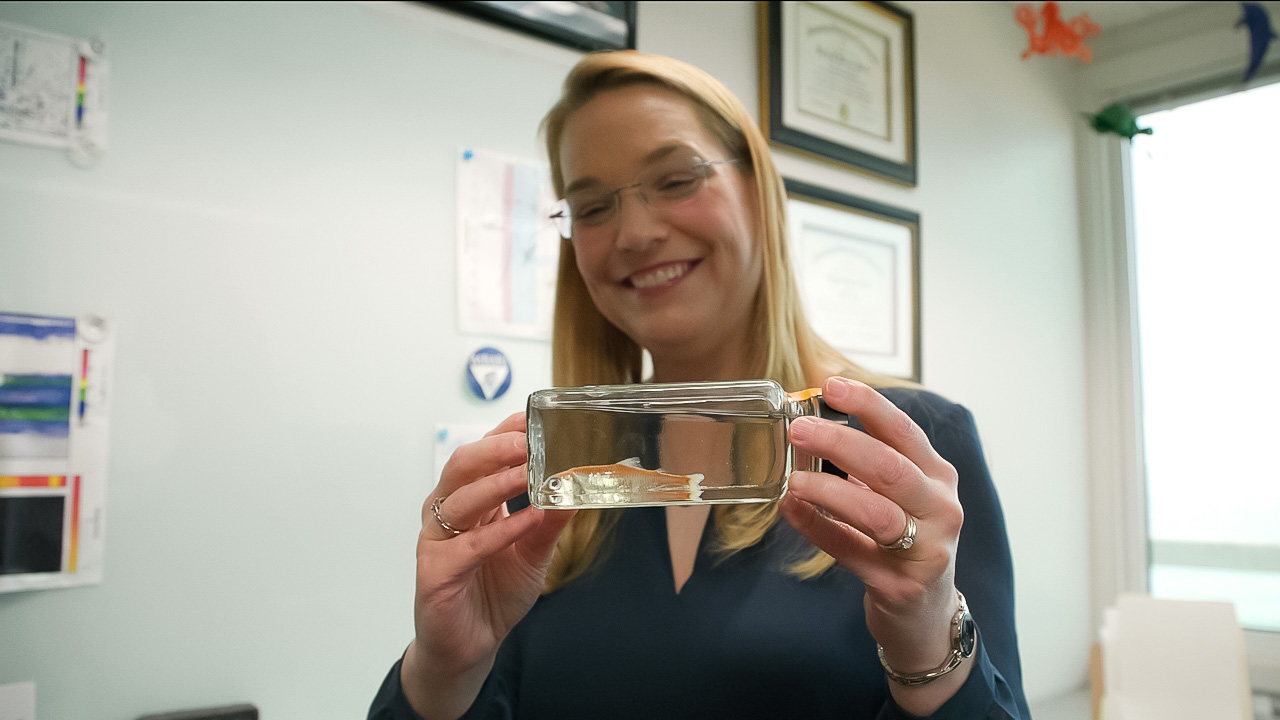 A woman holds a small jar containing a preserved fish