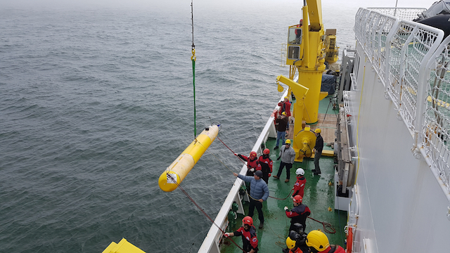 Marine operations crew launch a torpedo-shaped autonomous underwater vehicle off the side of a Korean icebreaker ship in the Arctic Ocean.