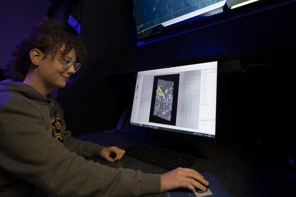 An intern sits at a computer in a dark video lab, manipulating a photomosaic collage of seafloor imagery.