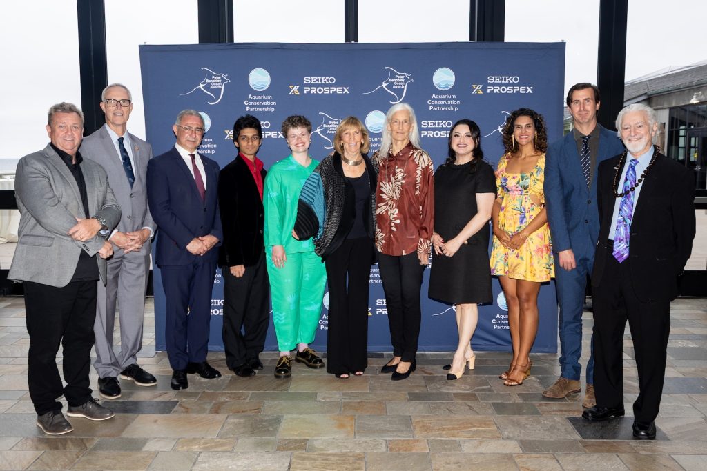 A group of 11 honorees and organizers for the 2026 Peter Benchley Ocean Awards pose for a photo. In the background is a large blue banner with the event name and logo, with sponsor names and logos.
