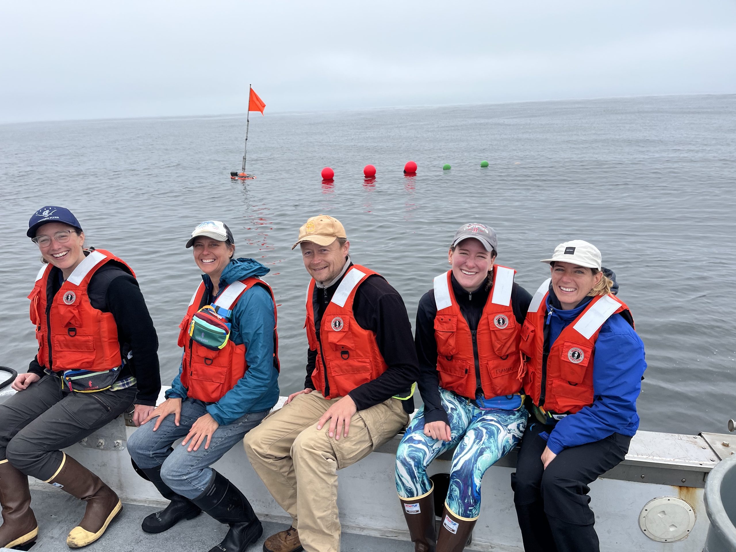Five members of the Carbon Flux ecology team onboard the Paragon with a drifting sediment trap in the water behind them.
