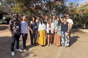 Twelve workshop participants pose for a photo outdoors on a sunny day in front of a grove of trees.