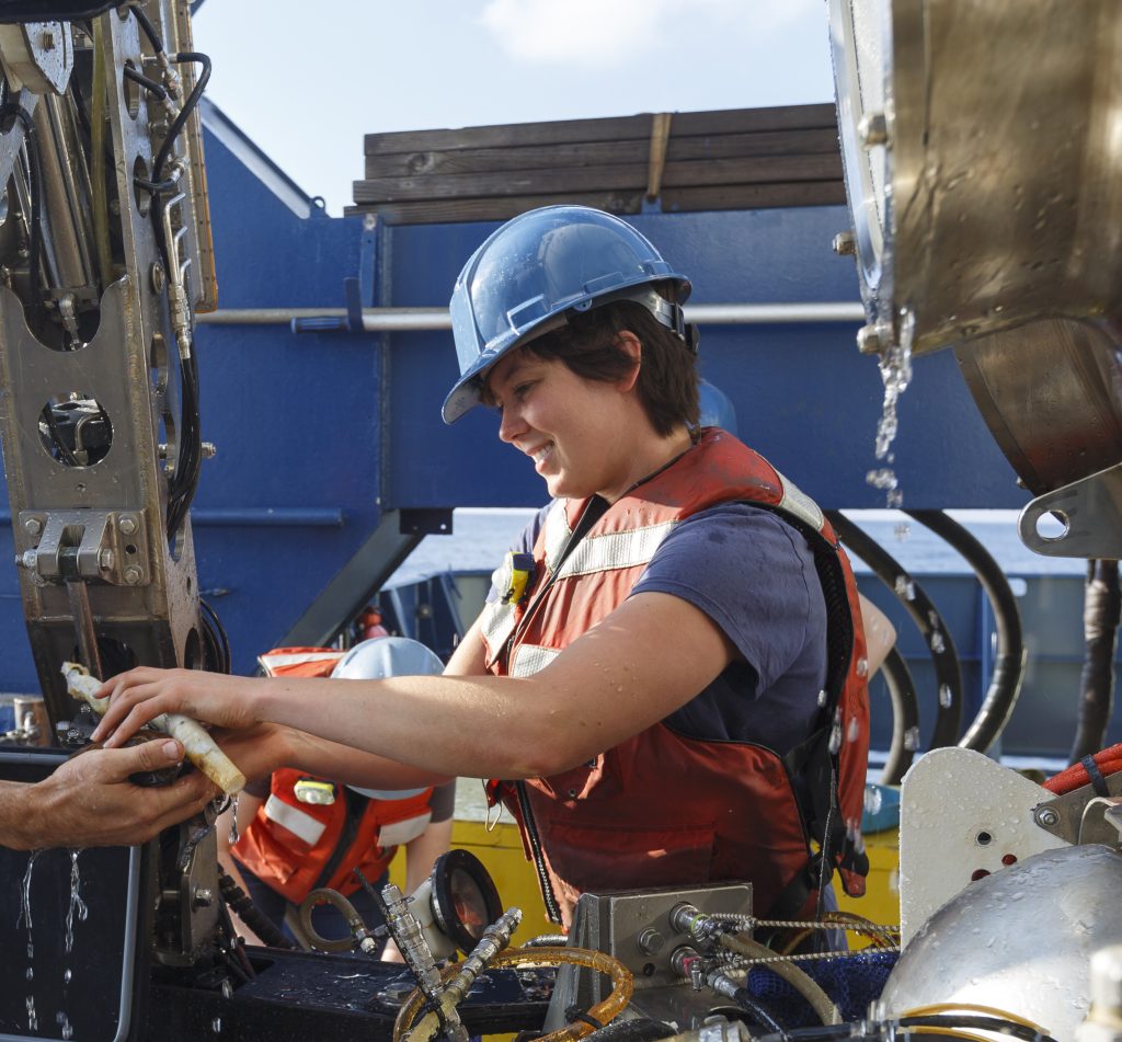 photo of Lauren Dykman in hard hat and life vest working on the HOV Alvin on the deck of a ship.