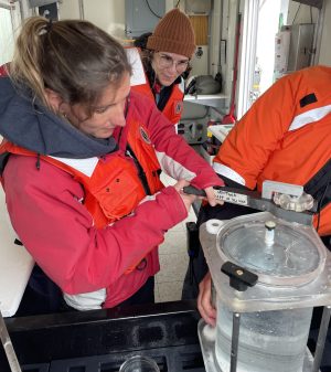 Emily in the lab onboard the R/V Rachel Carson watching postdoc Natalia Llopis Monferrer open a detritus sampler recovered from ROV Ventana.