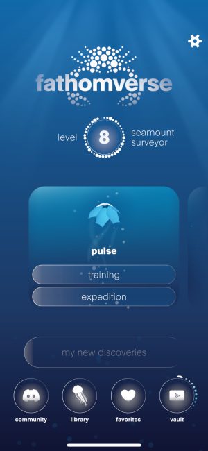 The hub screen of the FathomVerse mobile game displays a menu of game options. At the top is the FathomVerse logo with a crab made up of white dots of varying sizes and the word fathomverse above the crab’s claws. Below is a ring with white circles with the number 8 and the word level to the left and the label seamount surveyor to the right. In the middle is a light-blue box with rounded corners containing a light-blue origami-shaped avatar, a swirl of multi-colored dots, and the word pulse. Below are two wide buttons with rounded corners and the words training and expedition. At the bottom is a semi-transparent button that reads my new discoveries, and four white icons: from left, a game console icon captioned with the word community, a jelly icon captioned with the word library, a heart icon captioned with the word favorites, and a playback icon captioned with the word vault. The background is blue with light blue and sun rays at the top fading to dark blue and swirling dots at the bottom.