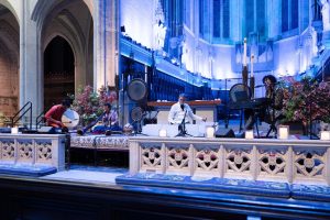 Four musicians seated in front of the altar of Grace Cathedral with musical instruments. The altar is illuminated with white and blue lights.