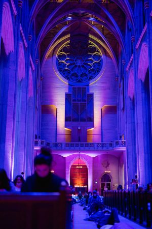 Sound bath participants seated in church pews and lying on the floor on yoga mats. The nave of Grace Cathedral is in the background and illuminated by purple light.