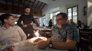 Two members of an expedition team enjoy dessert in a restaurant while a server lights a sparkling birthday candle.