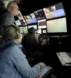 Scientists inside the ROV control room on the R/V Rachel Carson, looking at video monitors.