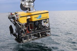A crane lifts a yellow robotic submersible out of the ocean.