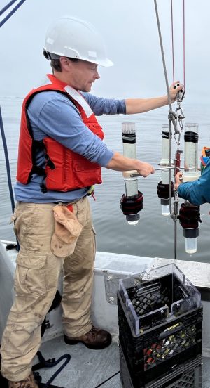 Scientists onboard a small boat holding a metal frame with collection tubes over the side of the boat.