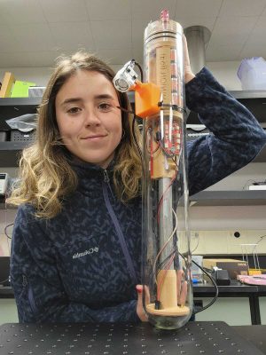 A scientist holding up a glass pill-shaped instrument