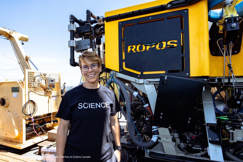 photo of Dr. Cherisse du Preez standing next to a ROV (ROPOS)